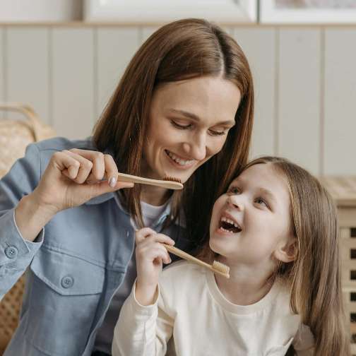 Mother teaches her daughter how to brush her teeth with sustainable tooth brushes
