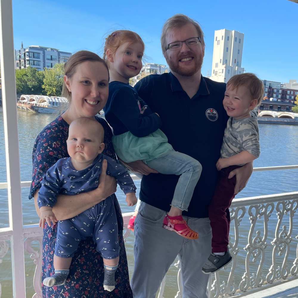 A man and his wife holding their three kids by the river. Kids are smiling and are happy