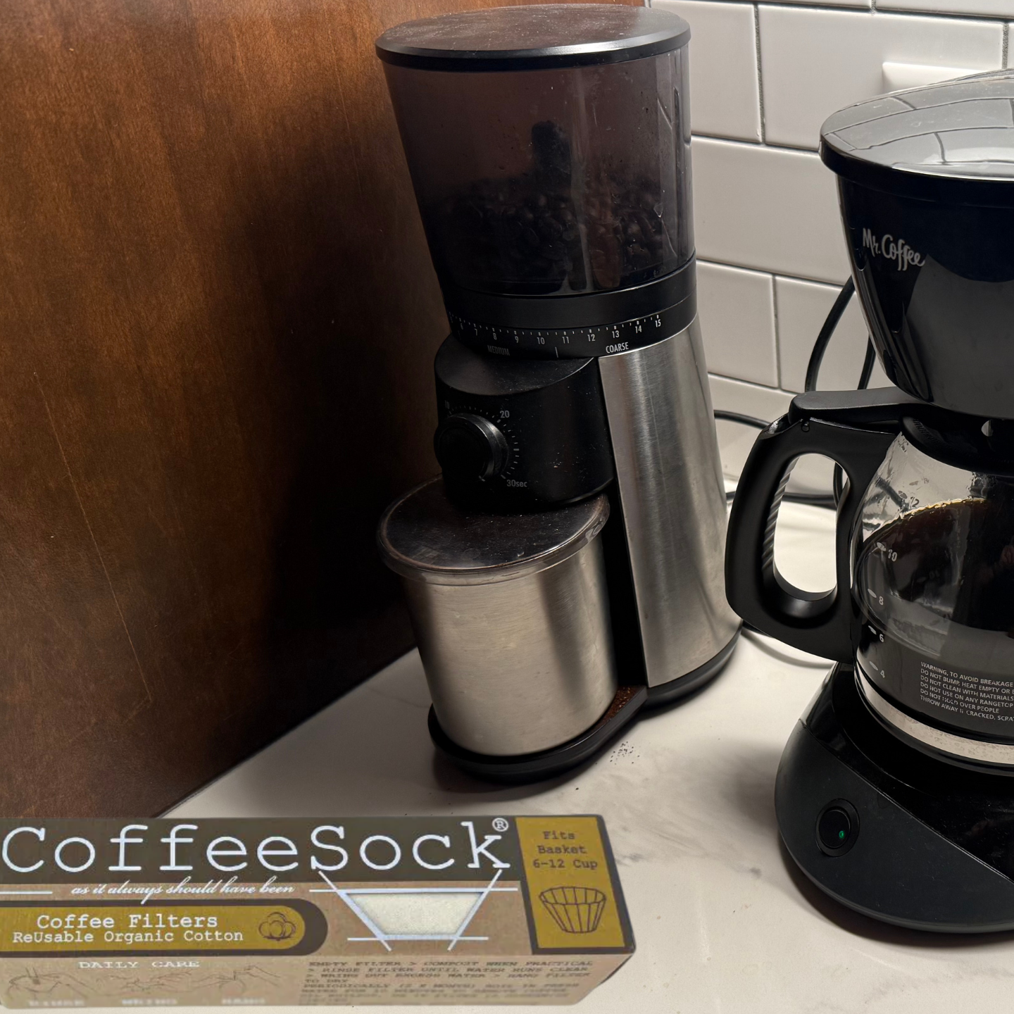 Black coffee maker on a kitchen counter with a box of CoffeeSock filters in the foreground.